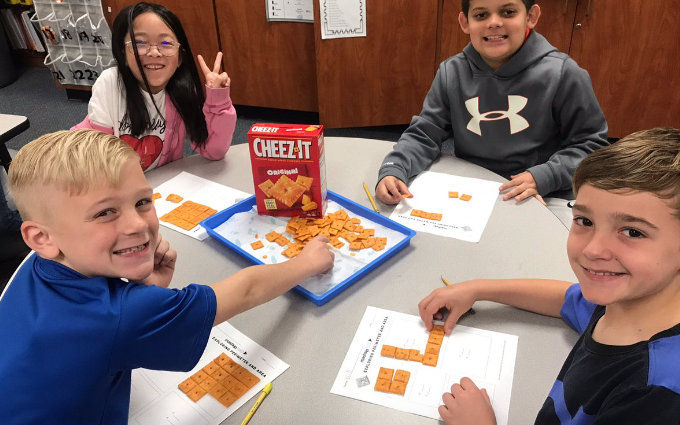 Kids gathered around a table measuring area on a worksheet with Cheez-it crackers 