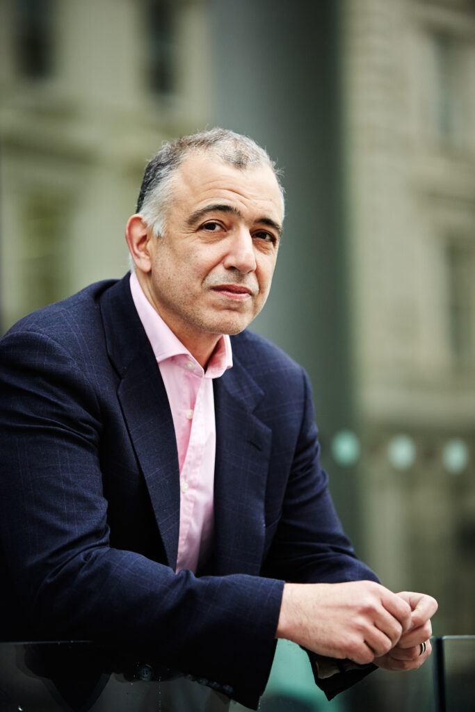 A man in his fifties is seen leaning over a railing looking pensive.