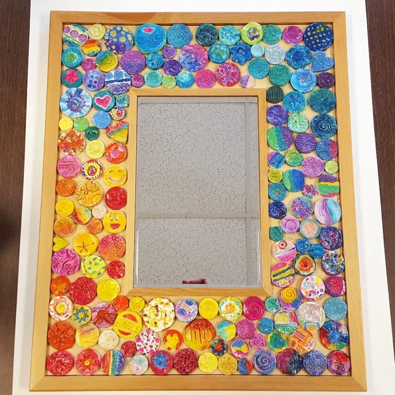 A mirror with a wide frame covered in clay mosaics made by students as an example of school auction art projects