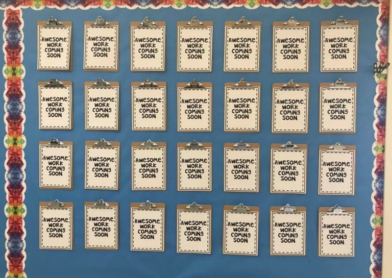 Bulletin board with clipboards attached, each holding a note saying "Awesome work coming soon"
