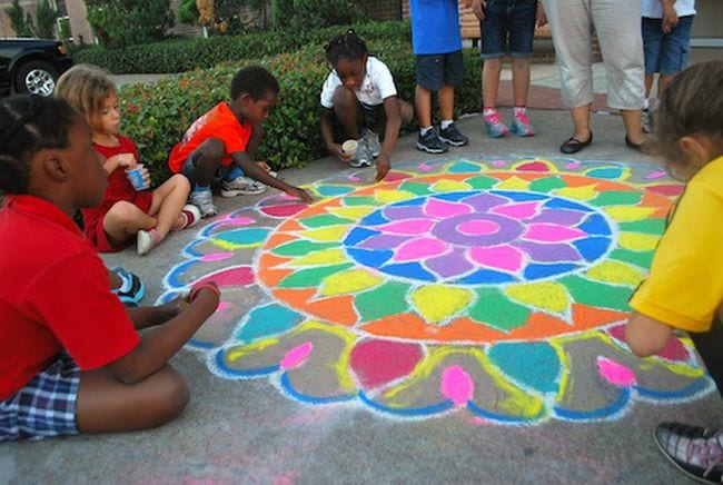 Students collaborating on a rangoli design made with chalk and sand