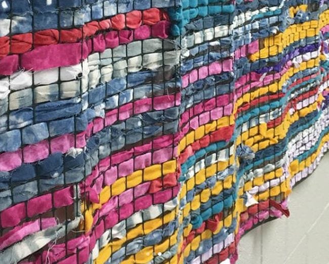 Fabric strips woven through chicken wire mounted on a wall in a wavy texture