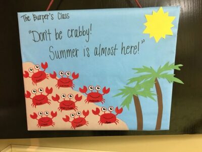 Bulletin board with a blue background, palm trees, and a sun saying 'Don't be crabby! Summer is almost here!' Each of the students names in the class are written on each of the crabs in the bottom corner. 