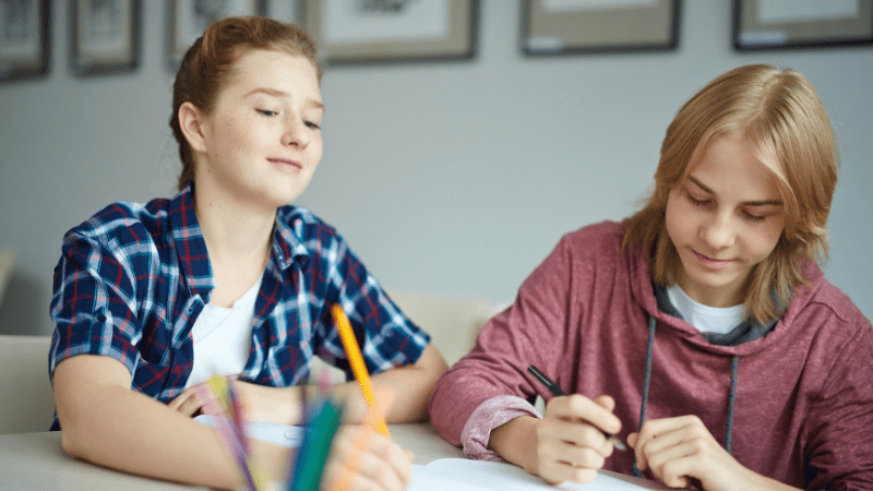Female and male teens drawing on paper on a desk