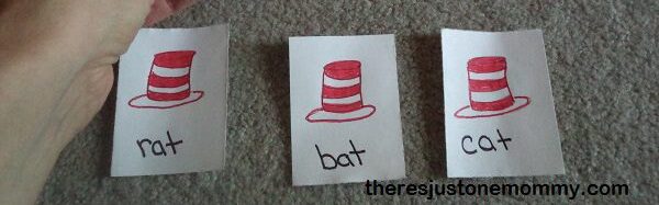 a child's hand holding a card with a red and white striped hat and the word fat other cards below