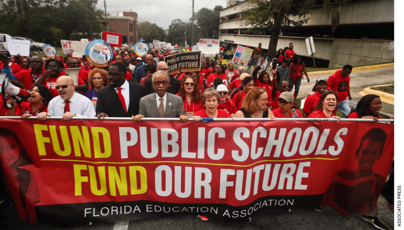 Florida education association teachers union members marching holding a sign that says fund public schools fund our future 