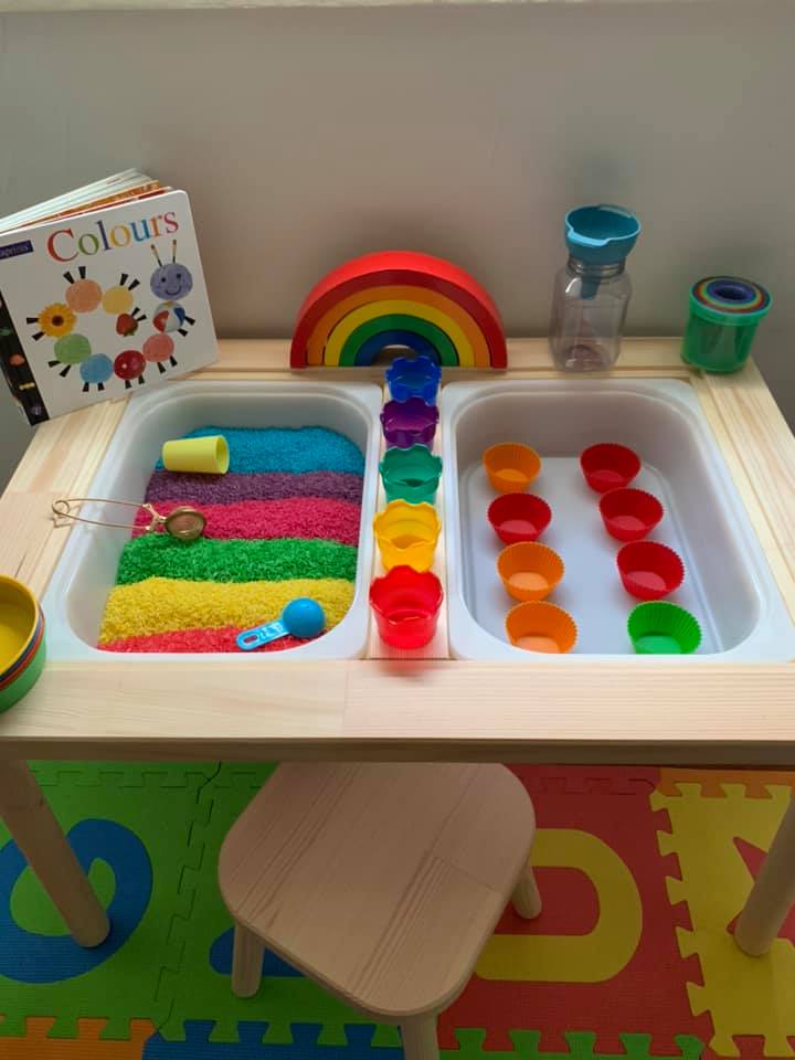 A table with two bins inside it is shown. There is rainbow sand on one side in this example of Ikea classroom.