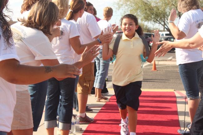 A young student walks down a red carpet giving high fives to other students as an example of first day of school activities