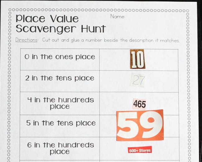 First grade math game worksheet labeled Place Value Scavenger Hunt with clues like 0 in the tens place, with numbers cut from magazines glued in place