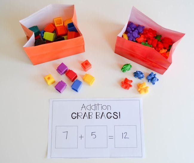 Colorful paper bags filled with math cubes and plastic bears used for first grade math games, with a worksheet called Addition Grab Bags