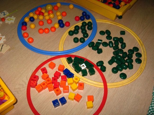 Large plastic hoops lying on the floor with math cubes, balls, and plastic beads sorted in them (First Grade Math Games)