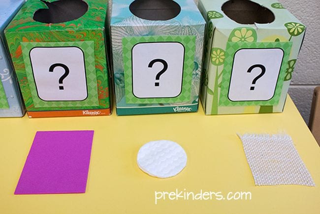 Tissue boxes with large questions marks on them, next to scraps of cloth and a cotton pad to teach the five senses