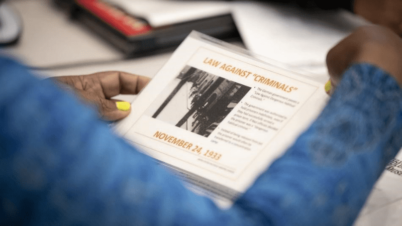 Image of Black teacher's hands holding a tablet with Holocaust information on it