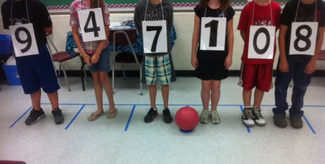 Students wearing numbers, lined up with a playground ball used to represent a decimal (Fourth Grade Math Games)
