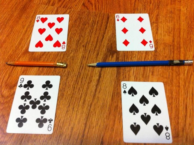 Four playing cards laid out on a table with a pencil between each vertical pair to represent fractions (Fraction Games)