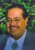 Color headshot of Francisco X. Alarcon with leaves in background.