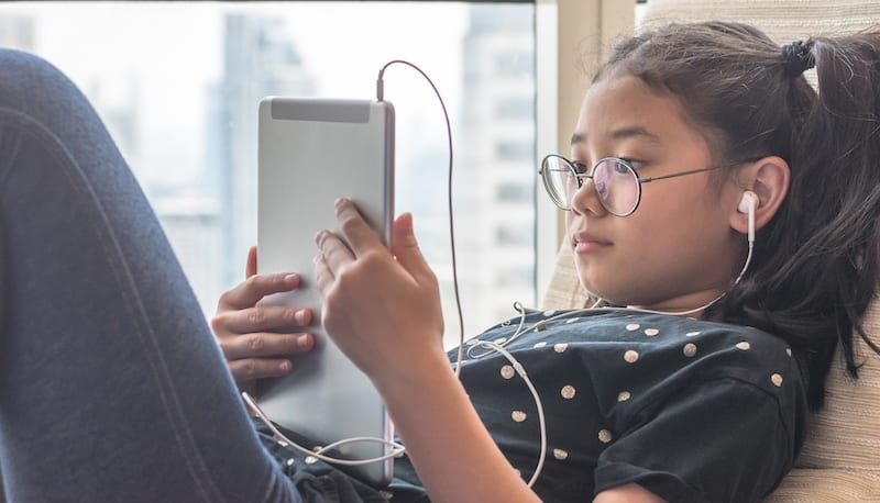 A child listening with earphones in connected to her tablet