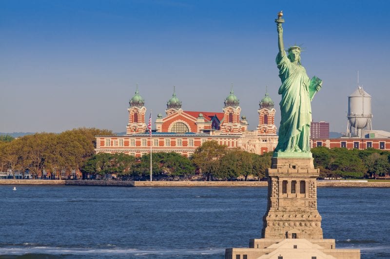 A close up of the Statue of Liberty with Ellis Island in the background