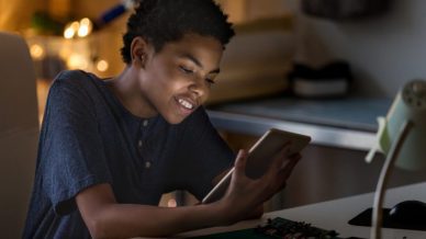 A young African American boy smiling at his tablet in the dark.