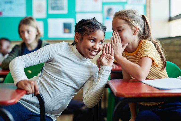 Shot of two young girls whispering to each other in a classroom
