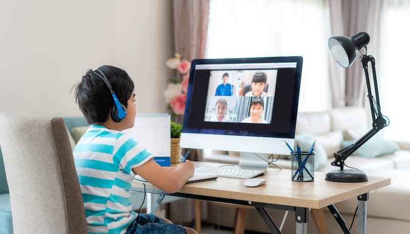 Asian boy student video conference e-learning with teacher and classmates on computer in living room at home.