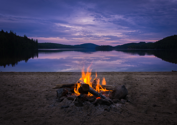 Summer camp activities include building a campfire like the one shown here in front of a body of water.