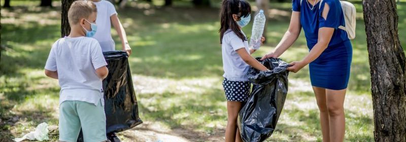 three children and one adult wearing masks in the woods cleaning up trash volunteering with children