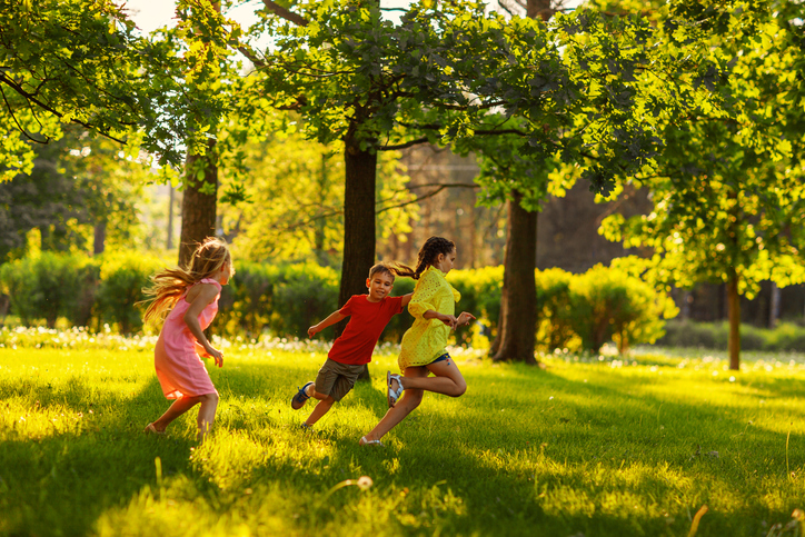 Three children are seen running in a field (tag games)