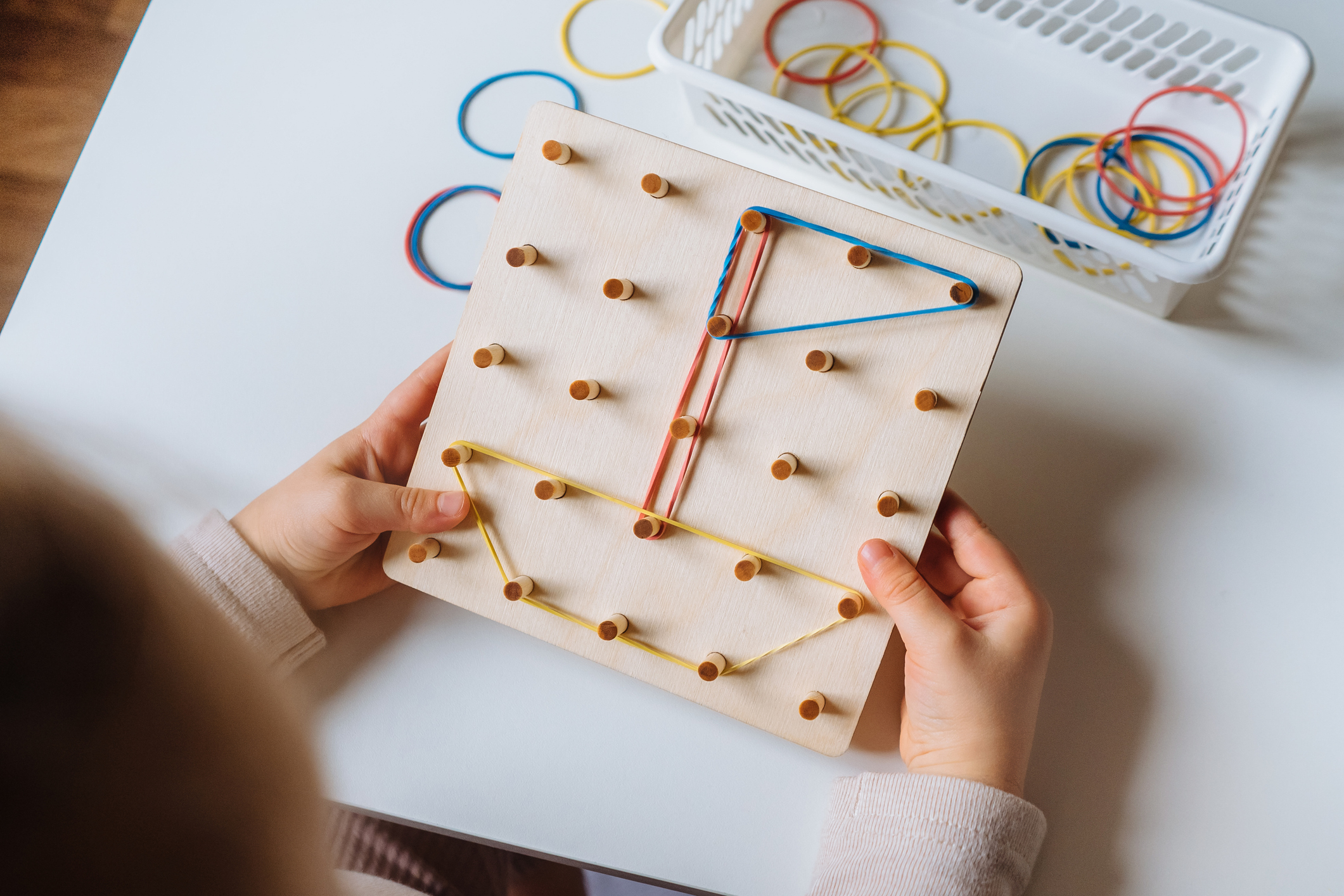 Child is playing with wooden geoboard at home. Children's creative game for early development and fine motor skills.