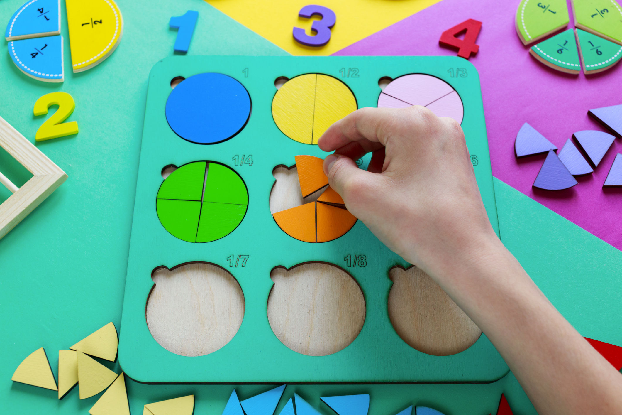 Kids hand moves wooden parts of fractions. Wooden toys on colorful paper. Educational fractions. Toys for kindergarten, preschool or daycare. Funny math game. Education in school. Top view
