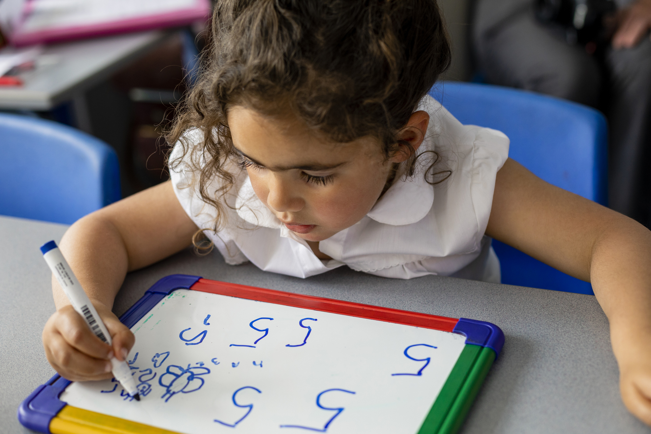 Primary school student sitting in a classroom writing on a mini whiteboard