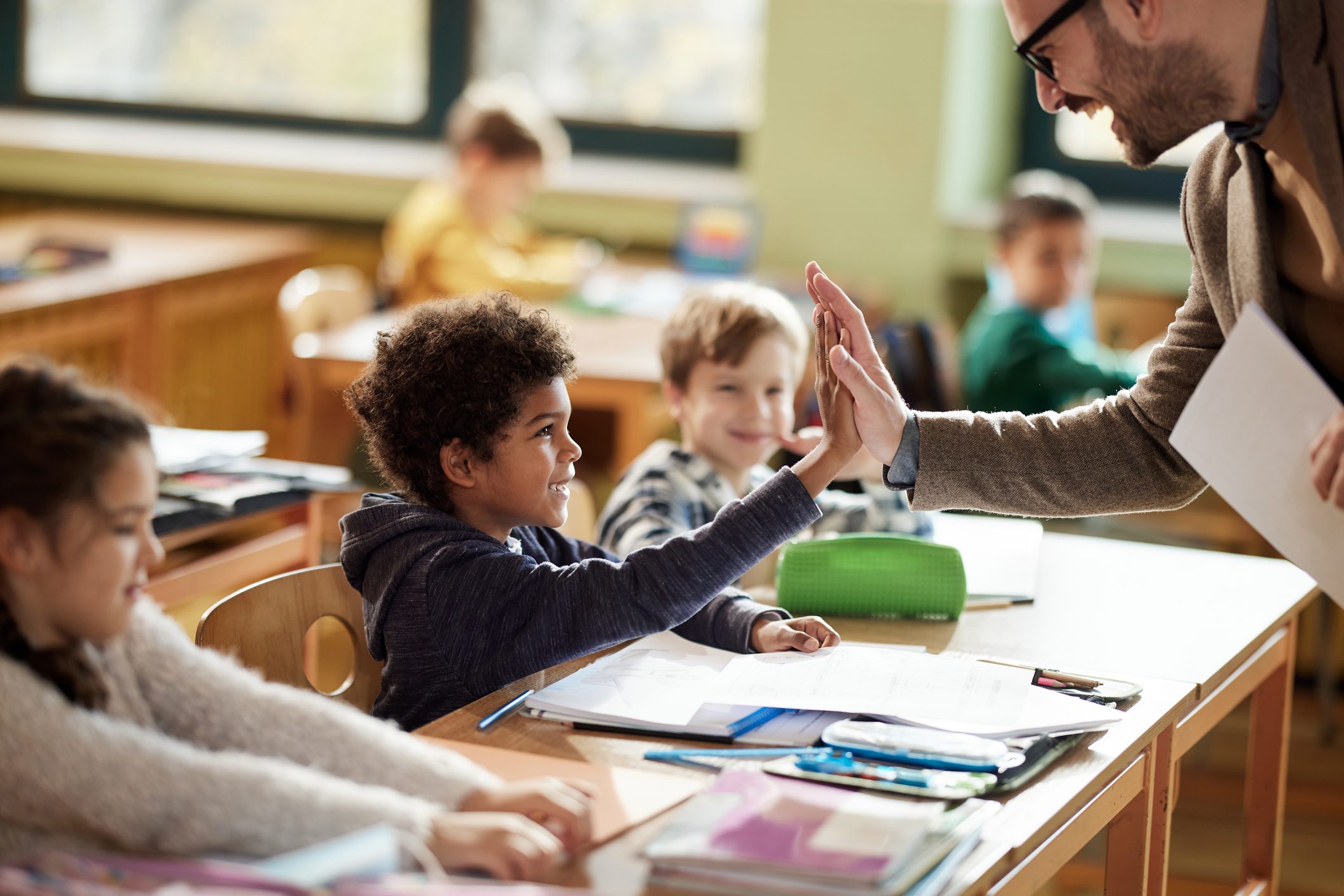 Happy male teacher giving high-five to his black elementary student on a class in the classroom.