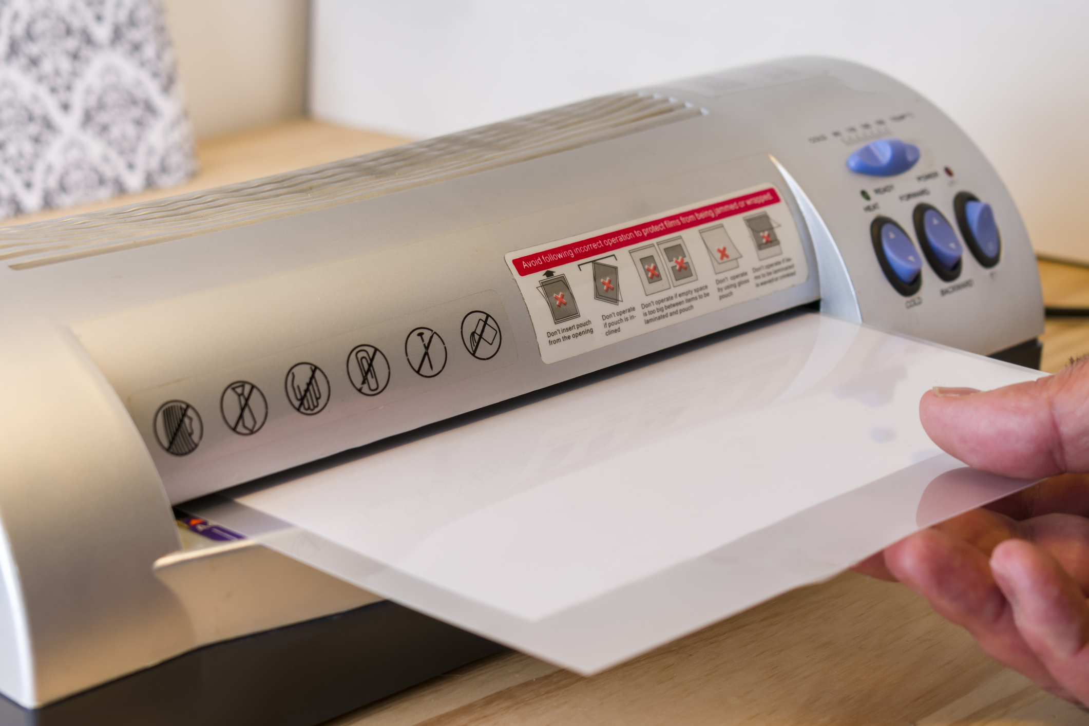 Hand holding a laminating pouch as it feeds into a laminator