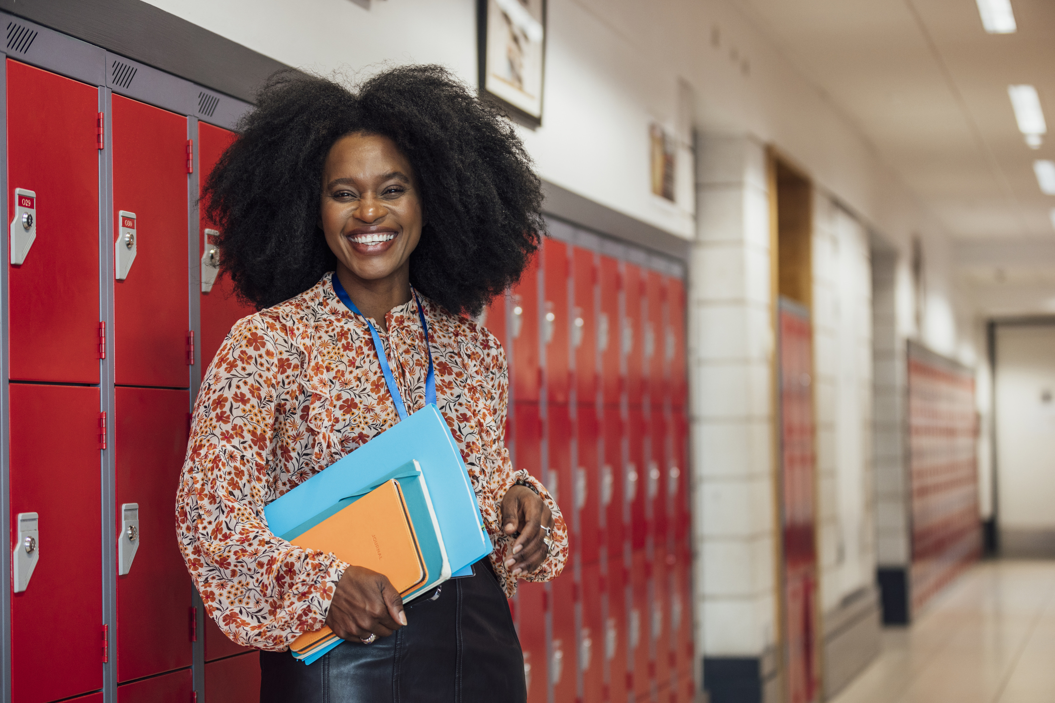 A woman standing in a corridor in the school that she works at in Gateshead, North East England. She is looking at the camera and smiling while holding a notebook.