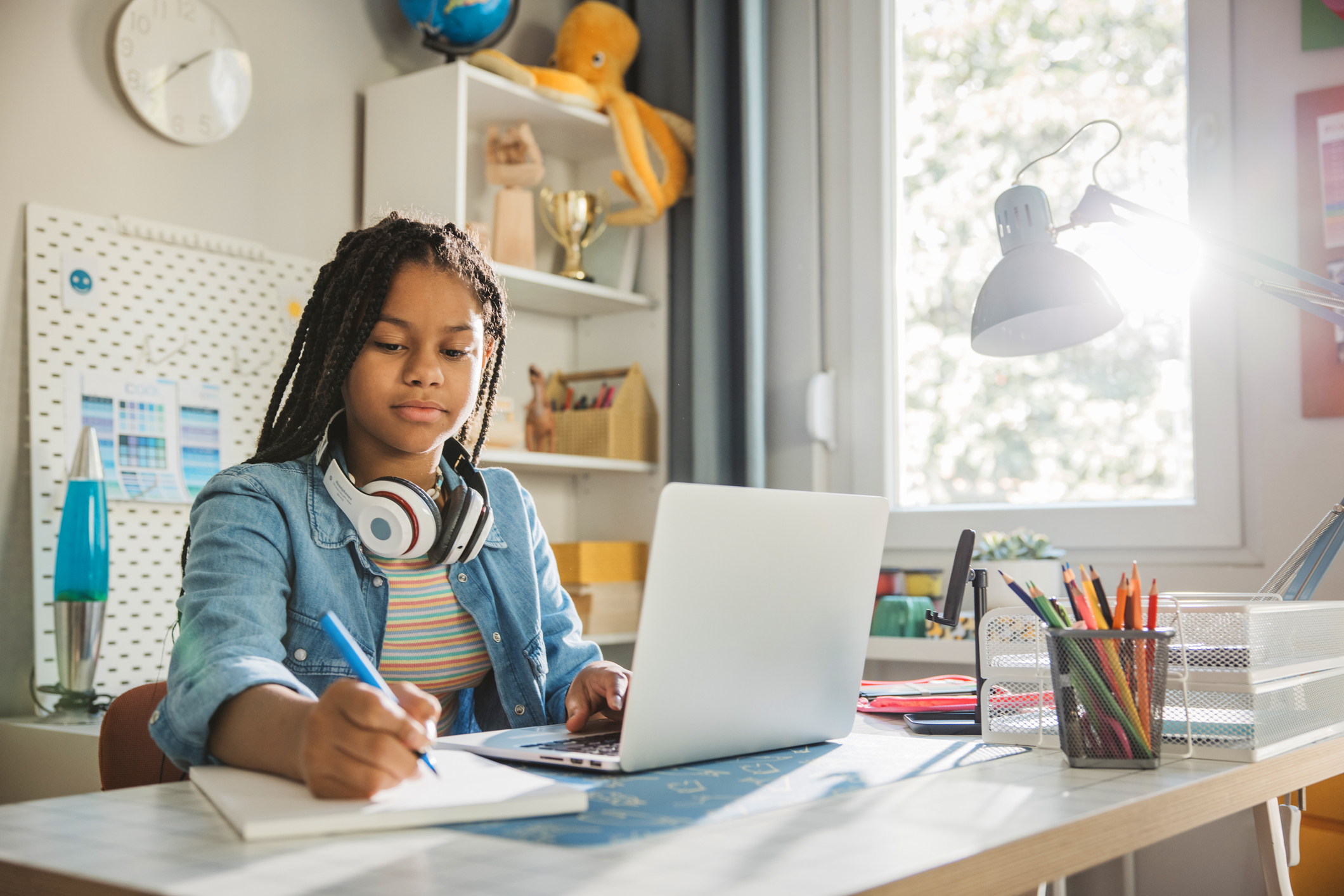 Teenage girl studding at home. She is sitting at the table and using laptop for homework.