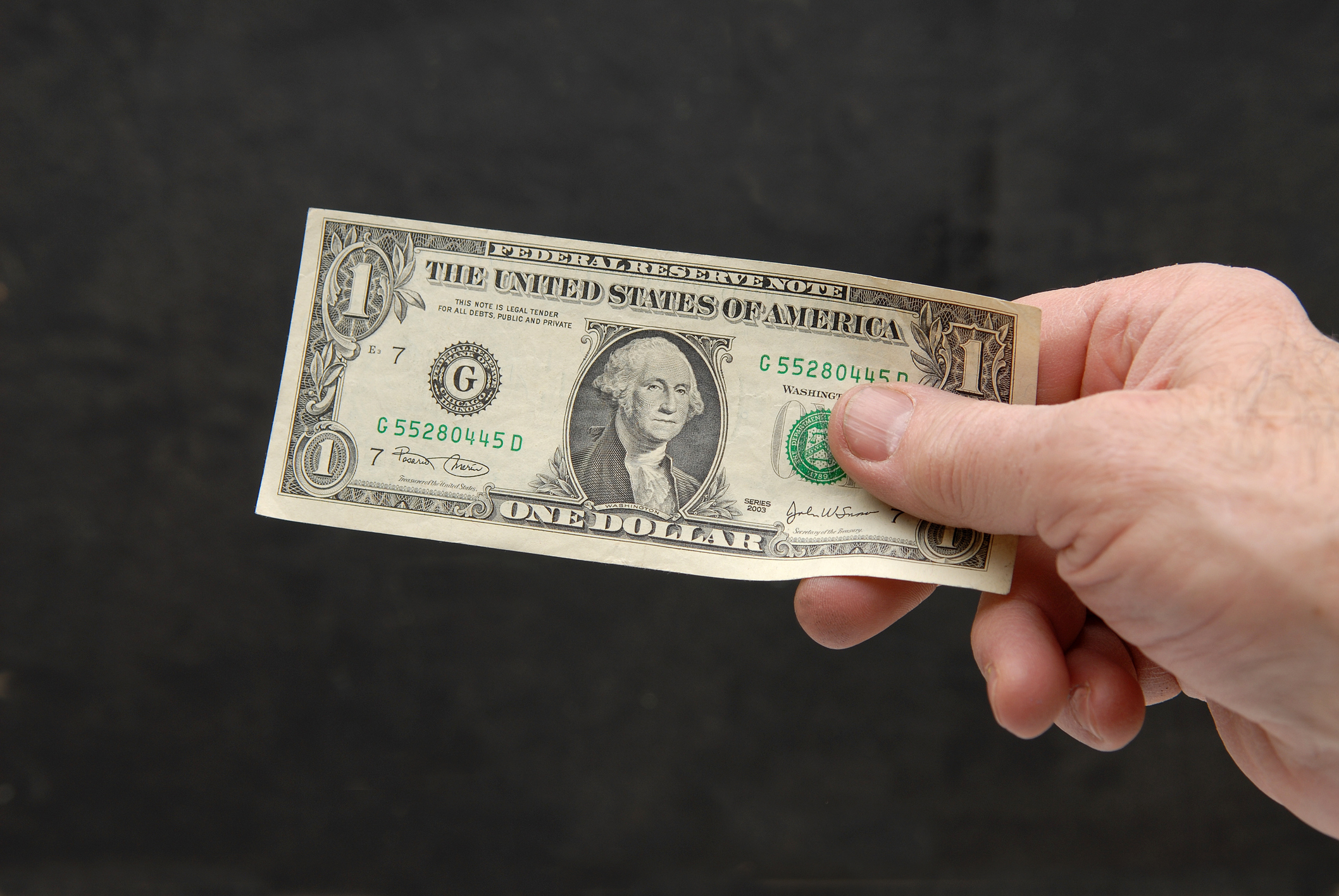 Hand holding a dollar bill against a black background