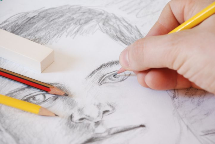 A hand is shown sketching a male face with a pencil (art careers)
