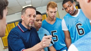 High school coach instructing basketball players in locker room