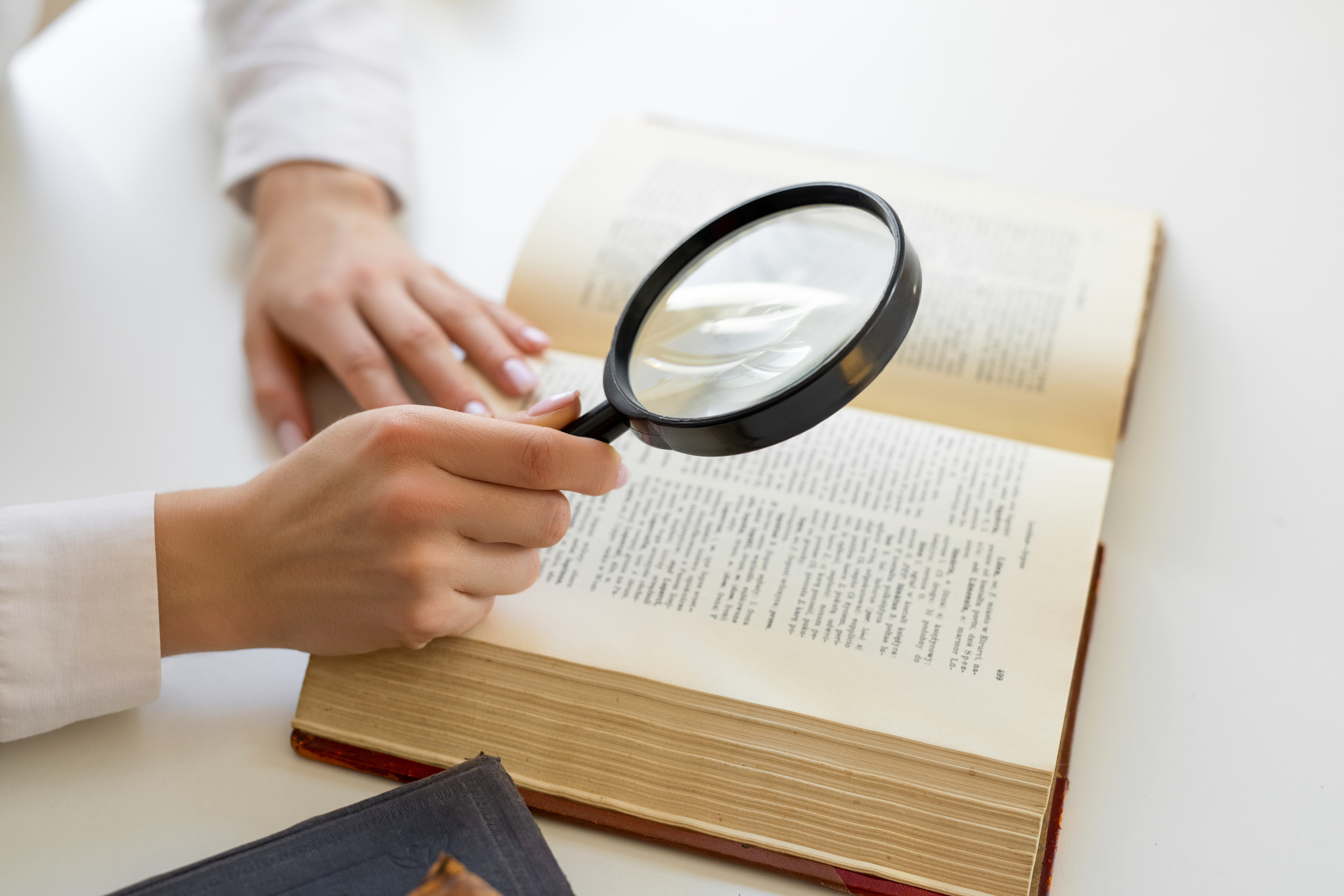 Woman's hand holding a magnifying glass over an open book