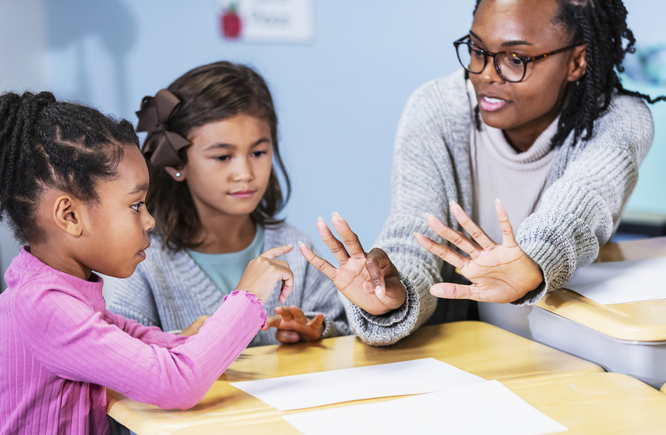 A black elementary teacher with children in the classroom. They are sitting at desks having a math lesson.