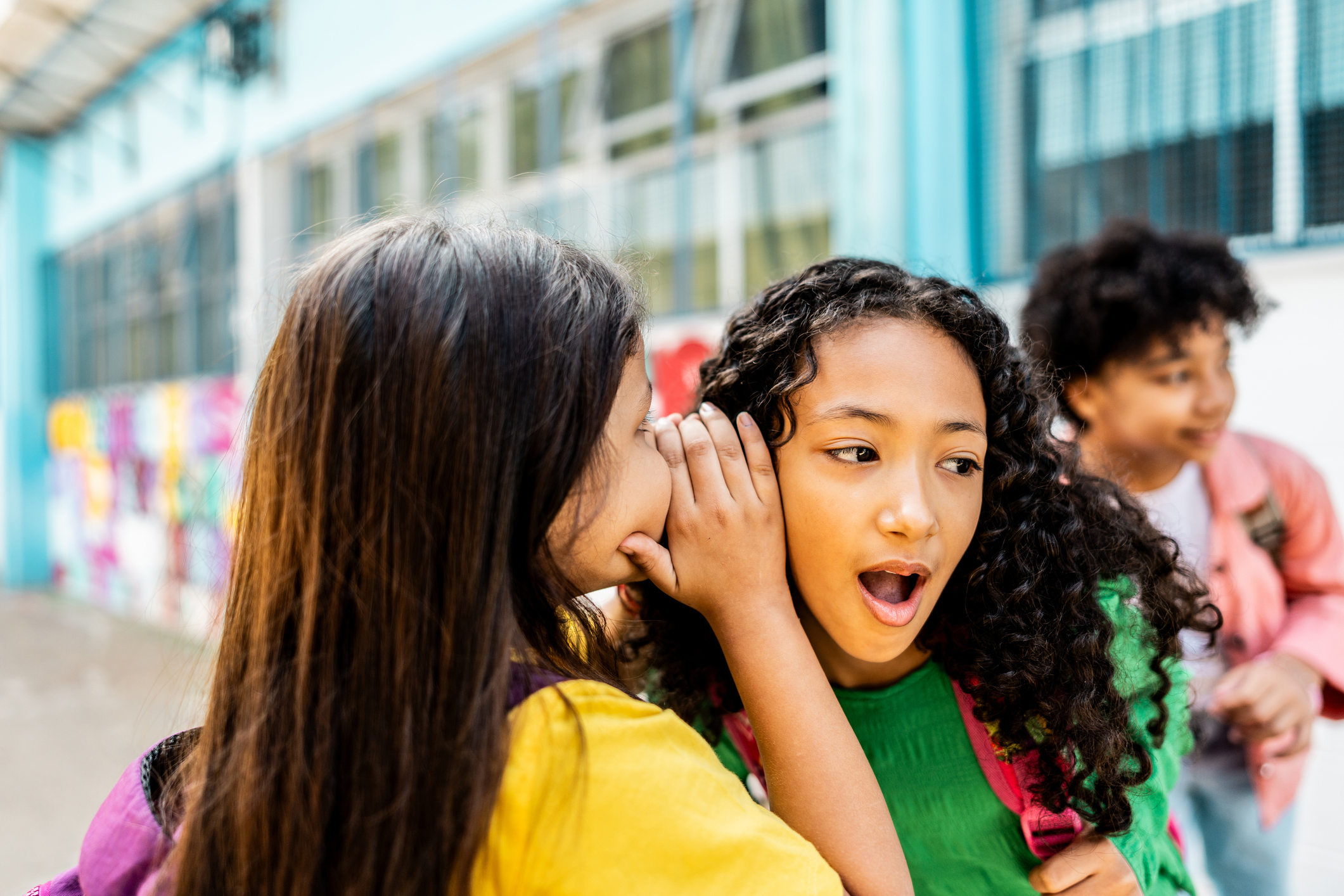 Schoolgirl whispering to friend on schoolyard