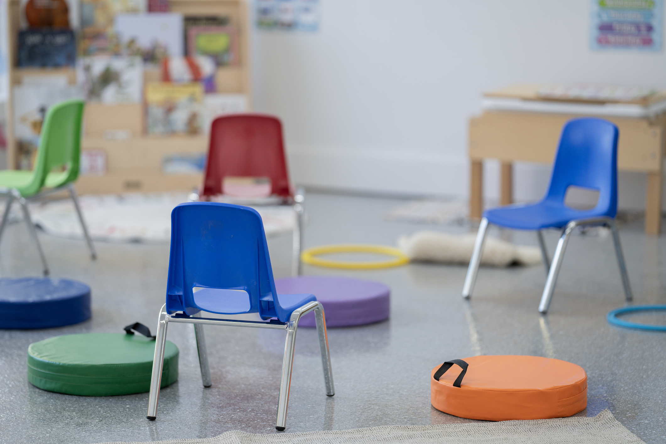 An empty daycare classroom ready for students. The class is full of colorful seats, chairs, books, toys and educational posters.