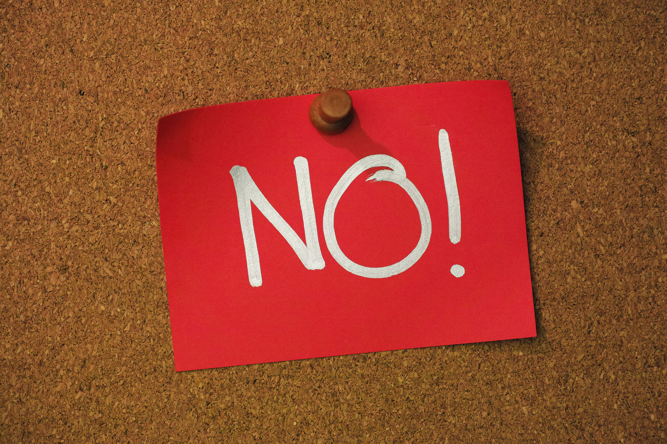 The word 'NO !' written in a silver marker pen on red note paper, pinned by a wooden pin to a cork message board. Conceptual message relating to no, deny, not allowed, cannot proceed, etc.