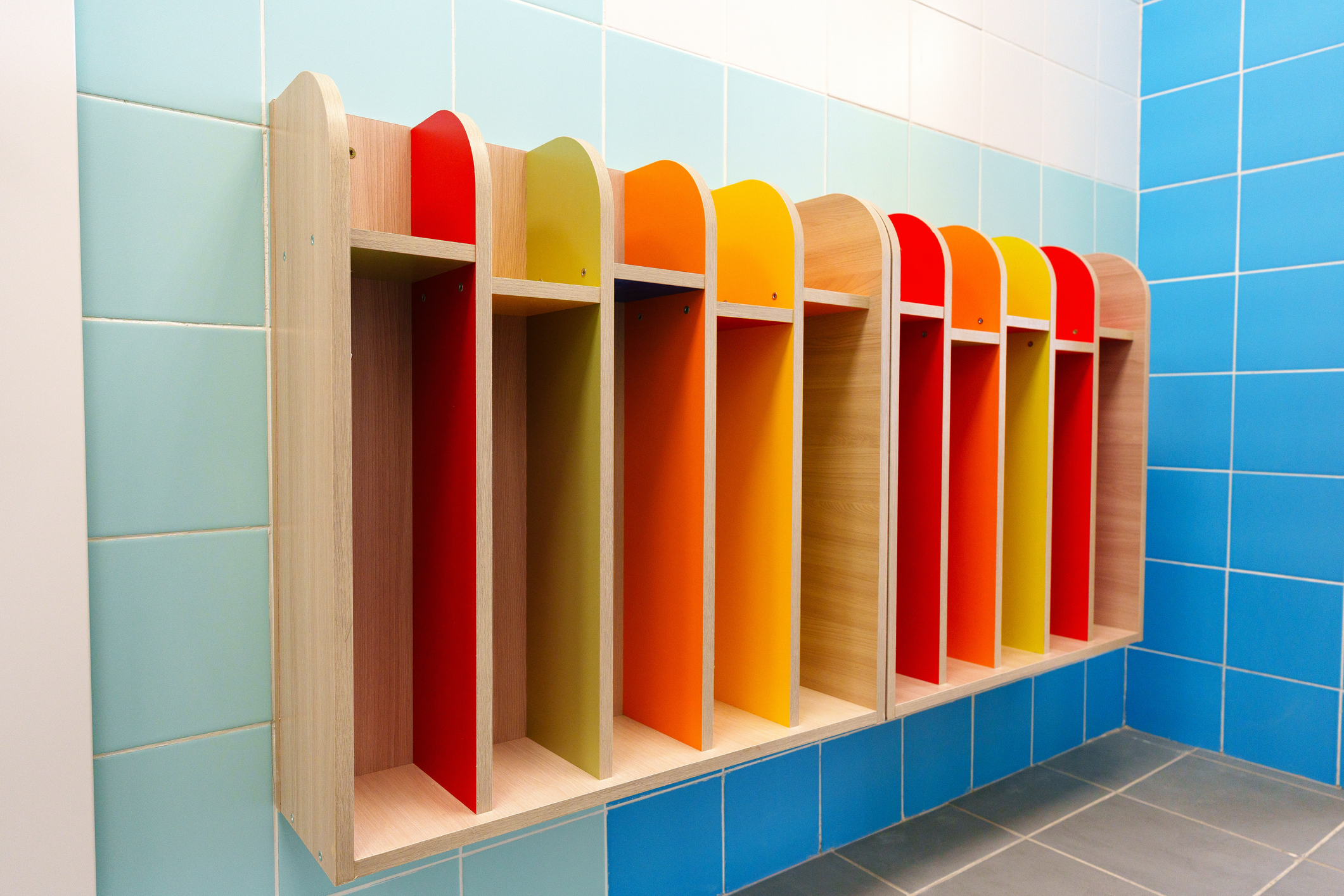 Wooden cubbies in vibrant colors are mounted on a wall, providing a neat solution for organizing items in a cheerful indoor environment, ideal for children.