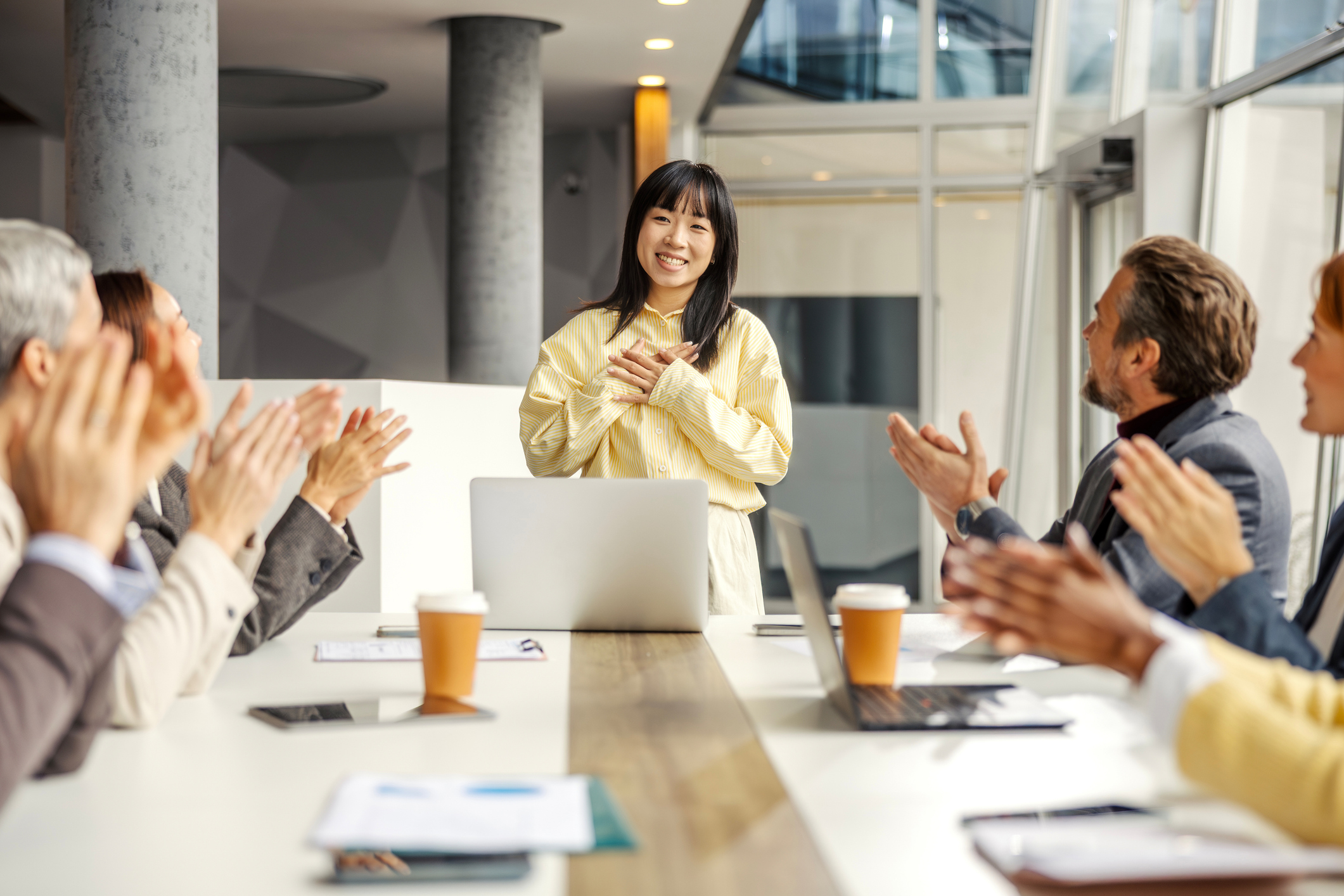 Confident young adult asian woman accepting respectful applause from her mixed age range business colleagues after a successful presentation or achievement in a modern office