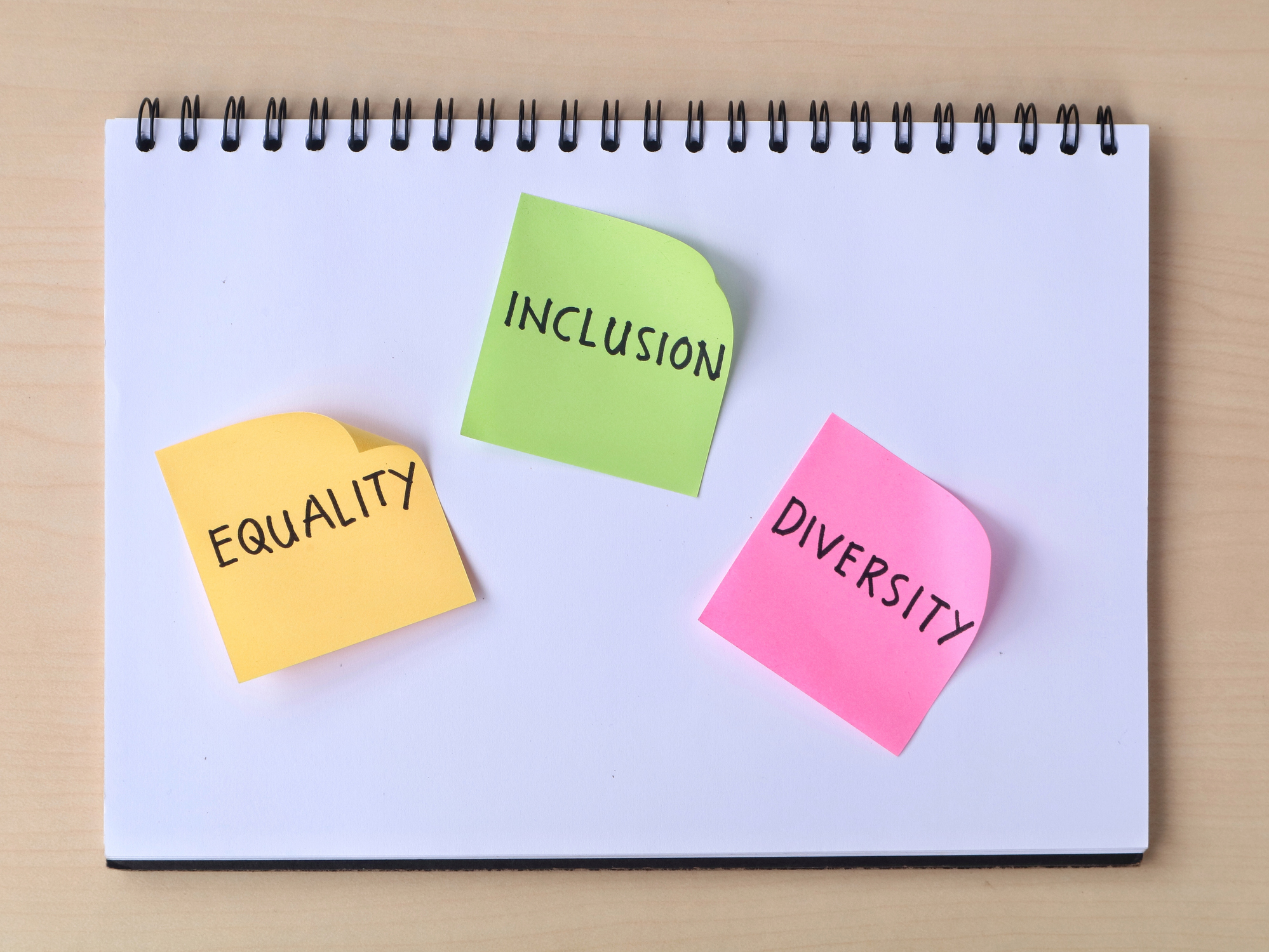 Equality, inclusion, and diversity words on colorful sticky notes in a notebook with wooden desk background. Top view