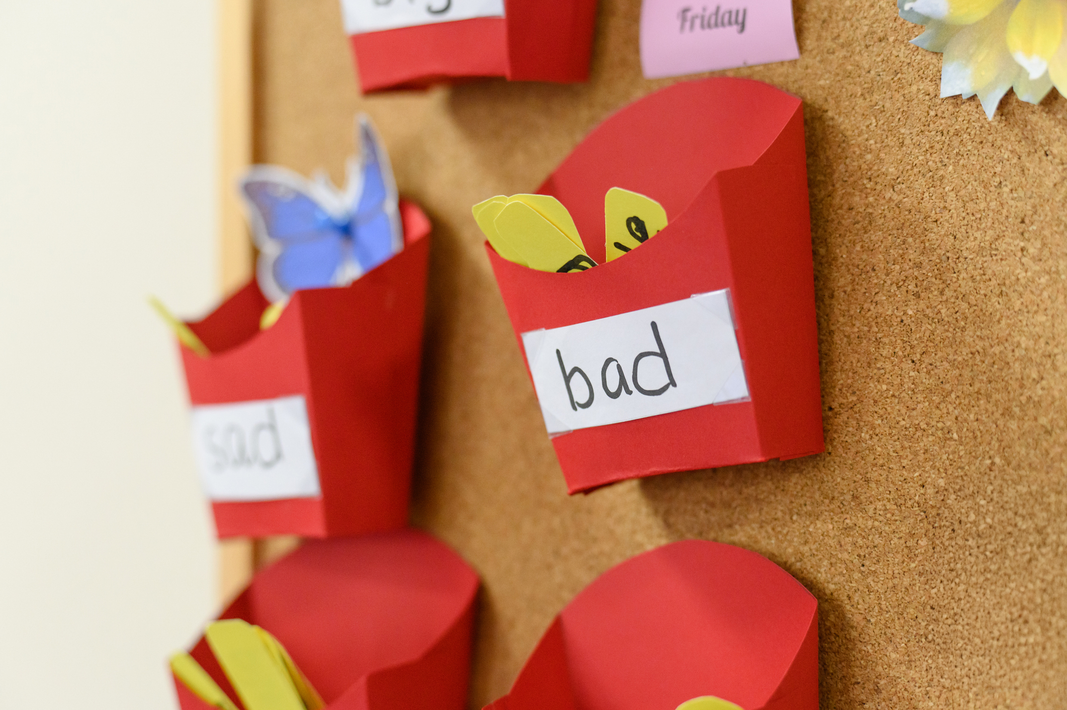 Brightly colored paper containers labeled with emotions like bad and sad attached to a corkboard, with decorative elements visible in the background