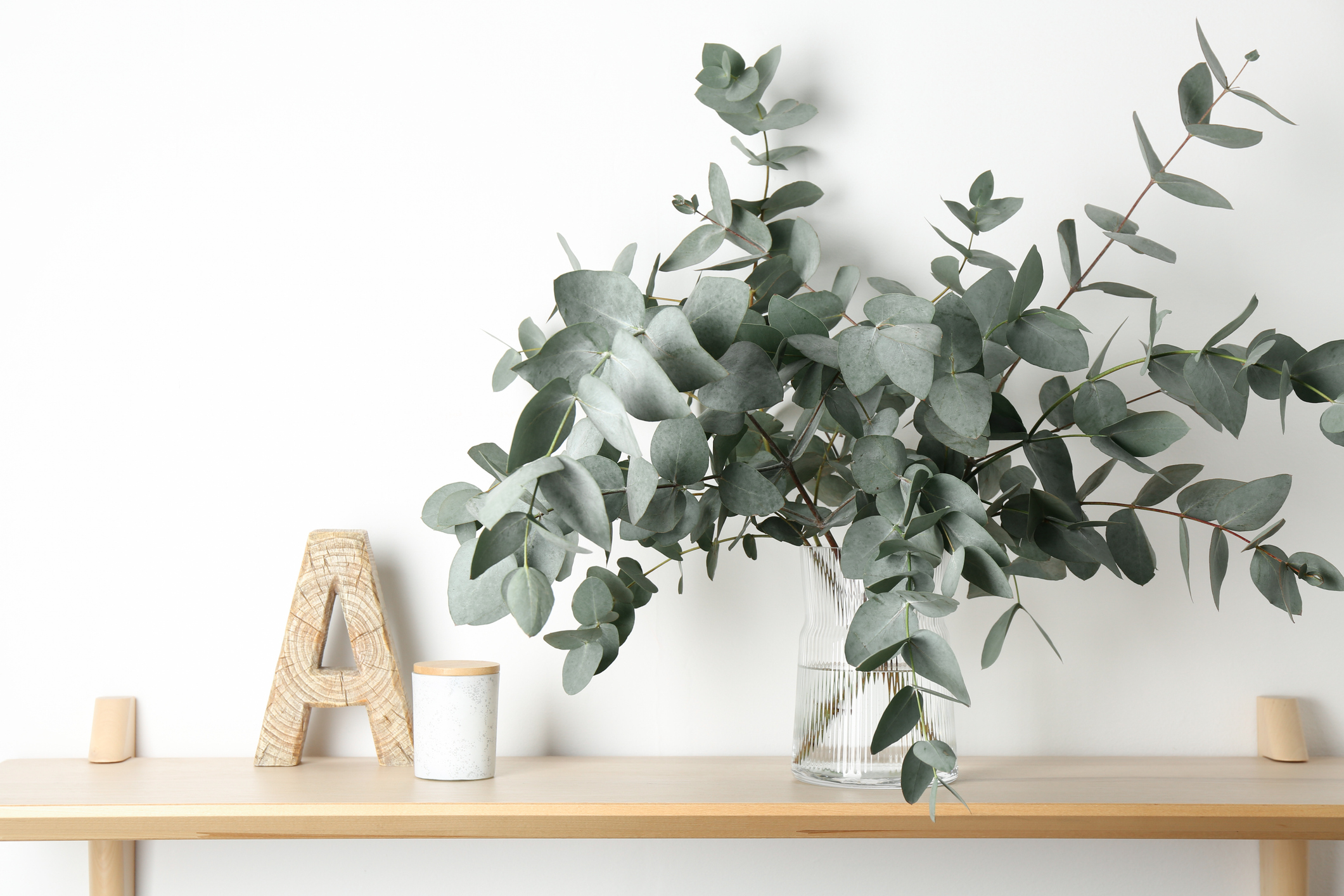 Beautiful eucalyptus branches in vase and other decor on wooden table near white wall indoors
