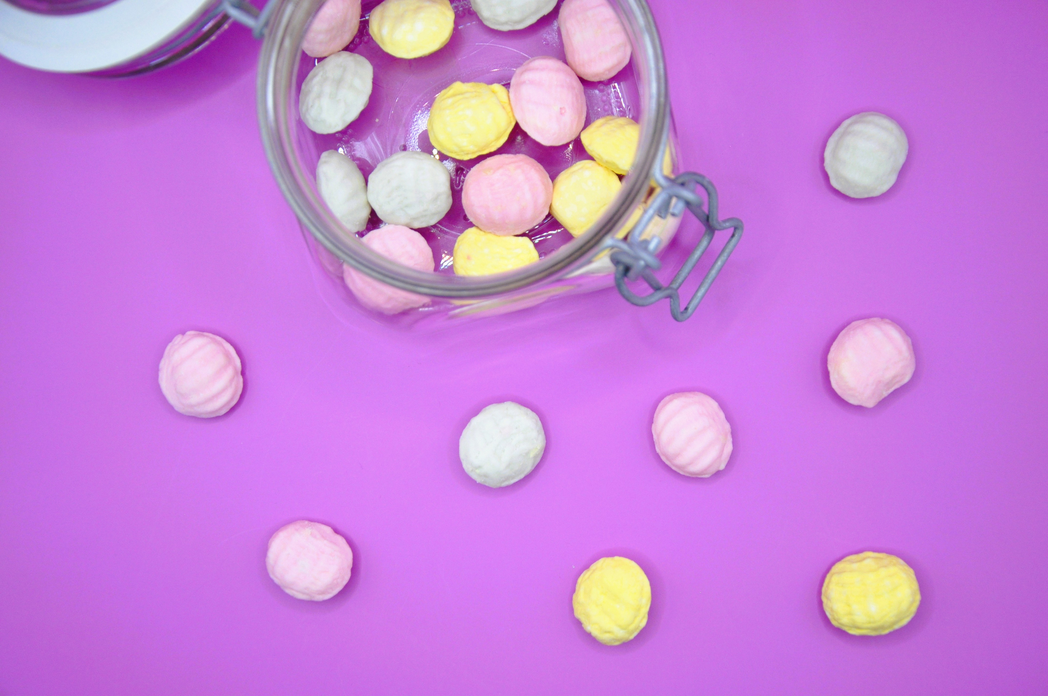 Loose pastel colored candies on a purple background with a glass jar holding additional candies