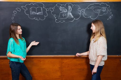 Students posing against a chalkboard with thought bubbles drawn with chalk.
